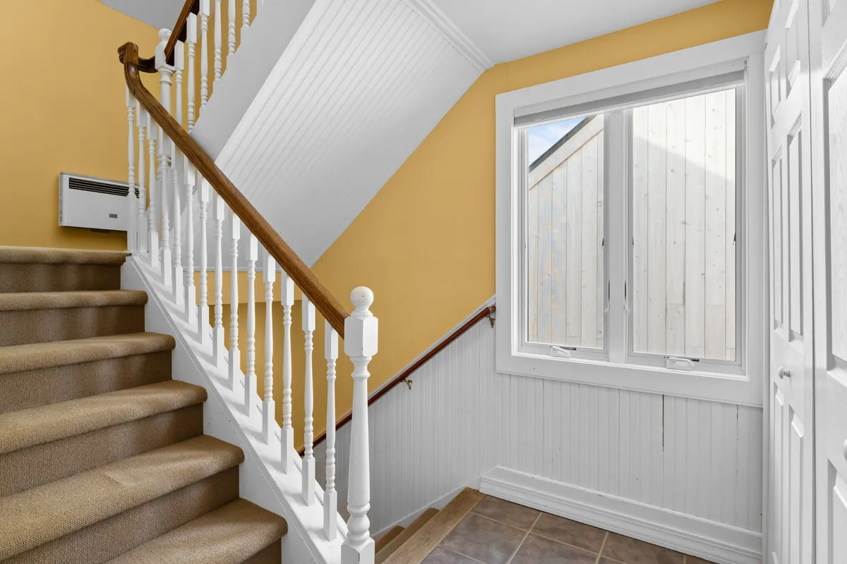 This image focuses on a staircase and a well-lit window, showcasing the home's vertical layout and the importance of safe movement between floors. The inviting mood and natural light make it appealing for families with children.