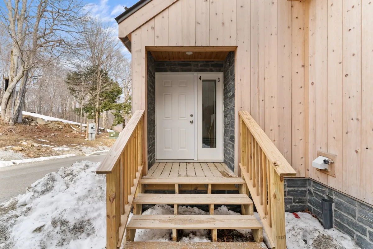 A close-up of the home's inviting entryway, with wooden stairs, a stone wall, and a welcoming front door. The porch provides a transitional space between the outdoors and indoors, highlighting the warmth and hospitality awaiting inside.