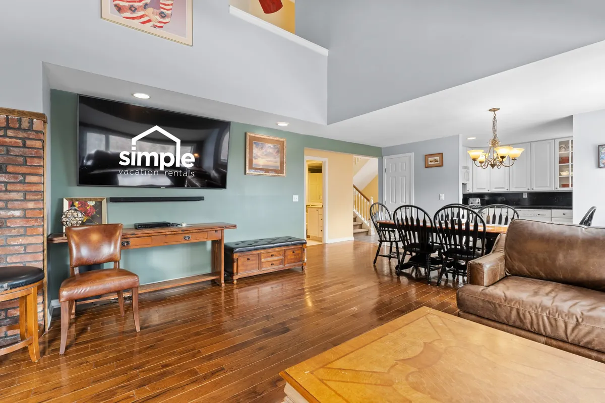 An open-concept living and dining area with a comfortable sofa, a wooden dining table, a television, and contemporary art pieces. The layout encourages both relaxation and socializing, embodying the heart-of-the-home feel described in the section.