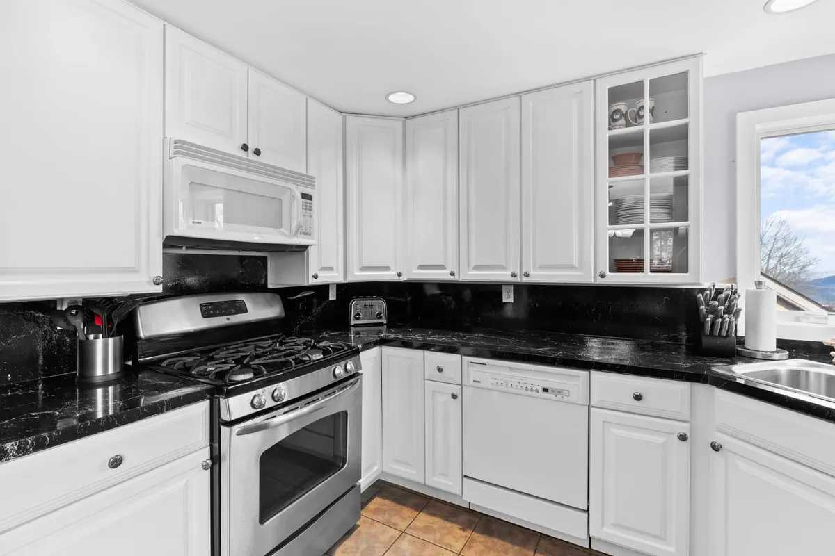 A modern kitchen featuring stainless steel appliances, black granite countertops, white cabinetry, and a glass-front cabinet. The space is designed for both cooking and socializing, with plenty of counter space and high-end finishes that invite culinary creativity.