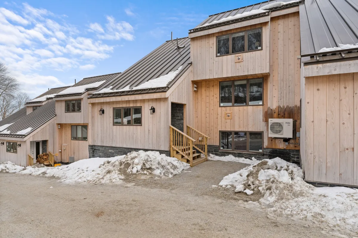 A welcoming exterior view of the property in winter, featuring wooden steps leading to the entrance, large windows aglow with light, and a snowy landscape. The porch offers a cozy spot to unwind after outdoor activities, and the setting invites gatherings and relaxation.