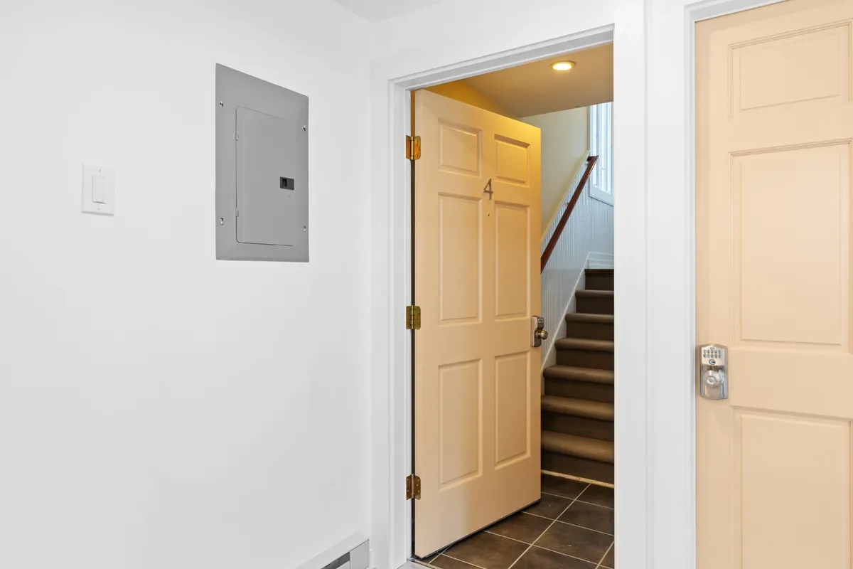 This image captures the open doorway and stairs leading up into the apartment, with an electrical panel visible. The view suggests a welcoming, transitional space where guests first enter, and hints at the multi-level layout that can be important for family logistics and safety.