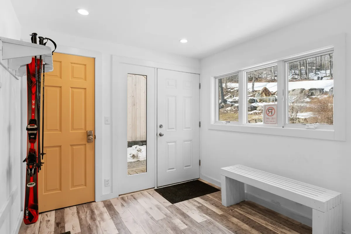 An inviting interior view featuring a bright yellow door, large windows that frame the snowy outdoors, and visible ski equipment. The entryway suggests a seamless transition between indoor comfort and outdoor adventure, reinforcing the connection to nature and trail activities described in the section.