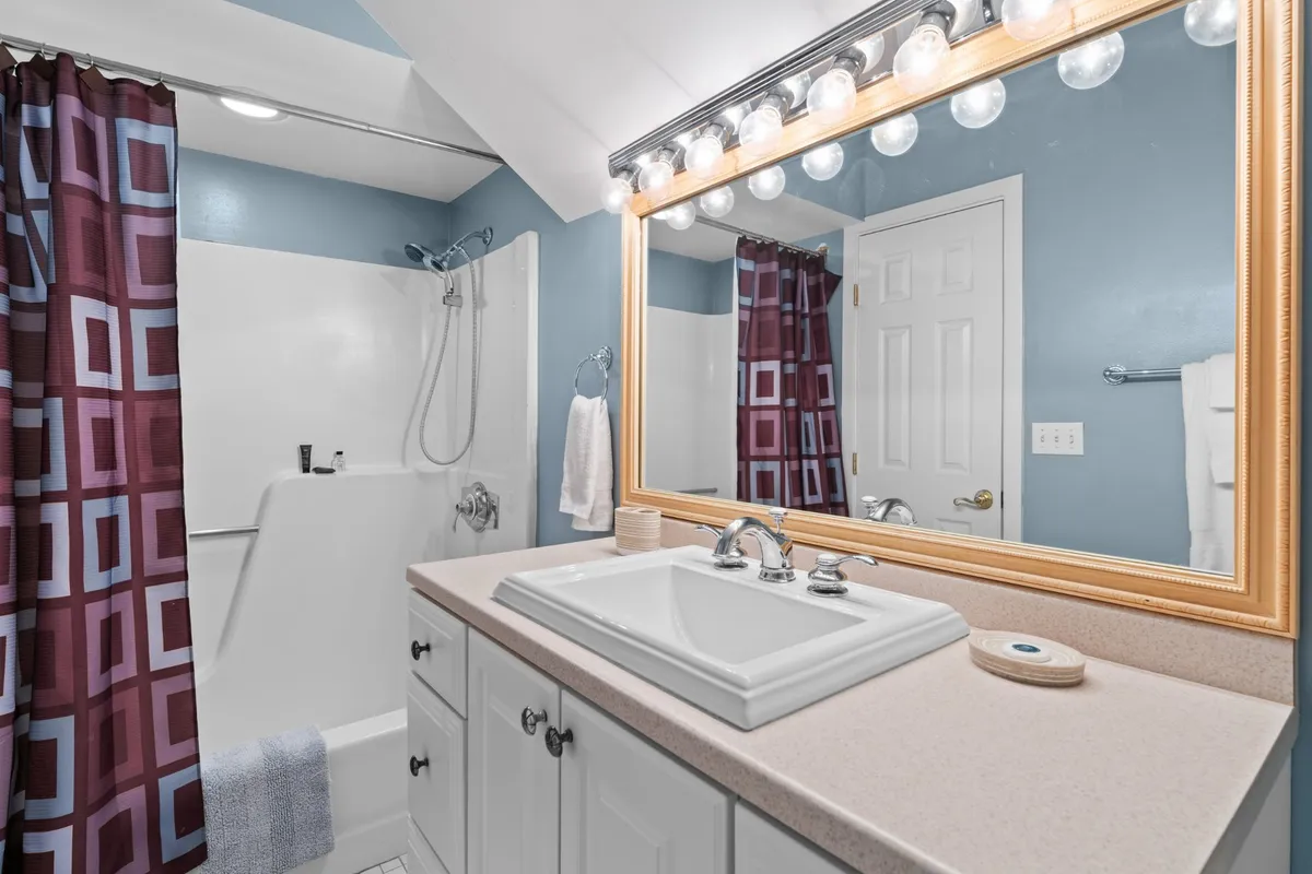A modern bathroom scene featuring a vanity sink, large mirror, and a colorful shower curtain over the shower area. The space is clean, refreshing, and thoughtfully designed, supporting routines like morning grooming or a relaxing shower after a day outdoors.
