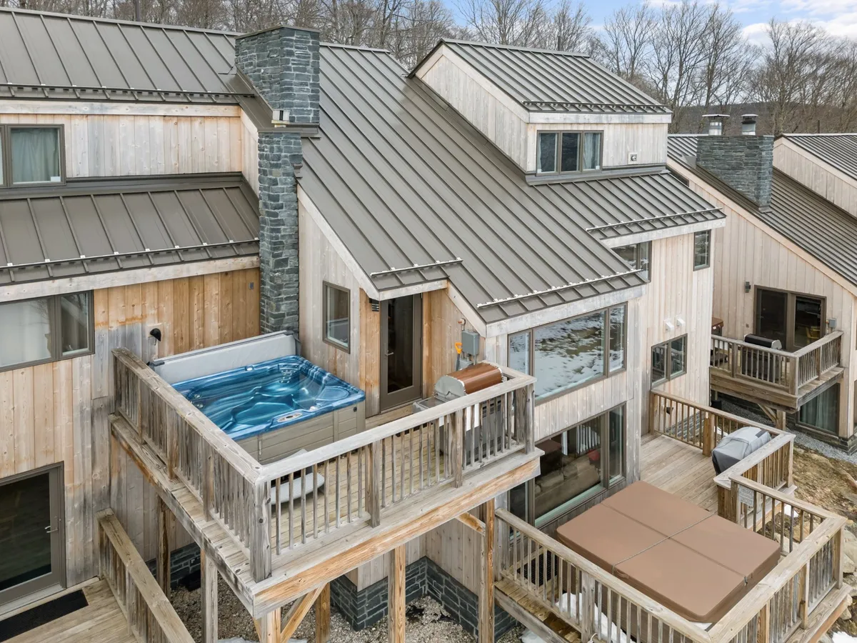 A spacious wooden deck featuring a hot tub, BBQ grill area, and a stone chimney, set against a backdrop perfect for sunset views and outdoor dining. The deck invites relaxation and social gatherings just outside the kitchen.
