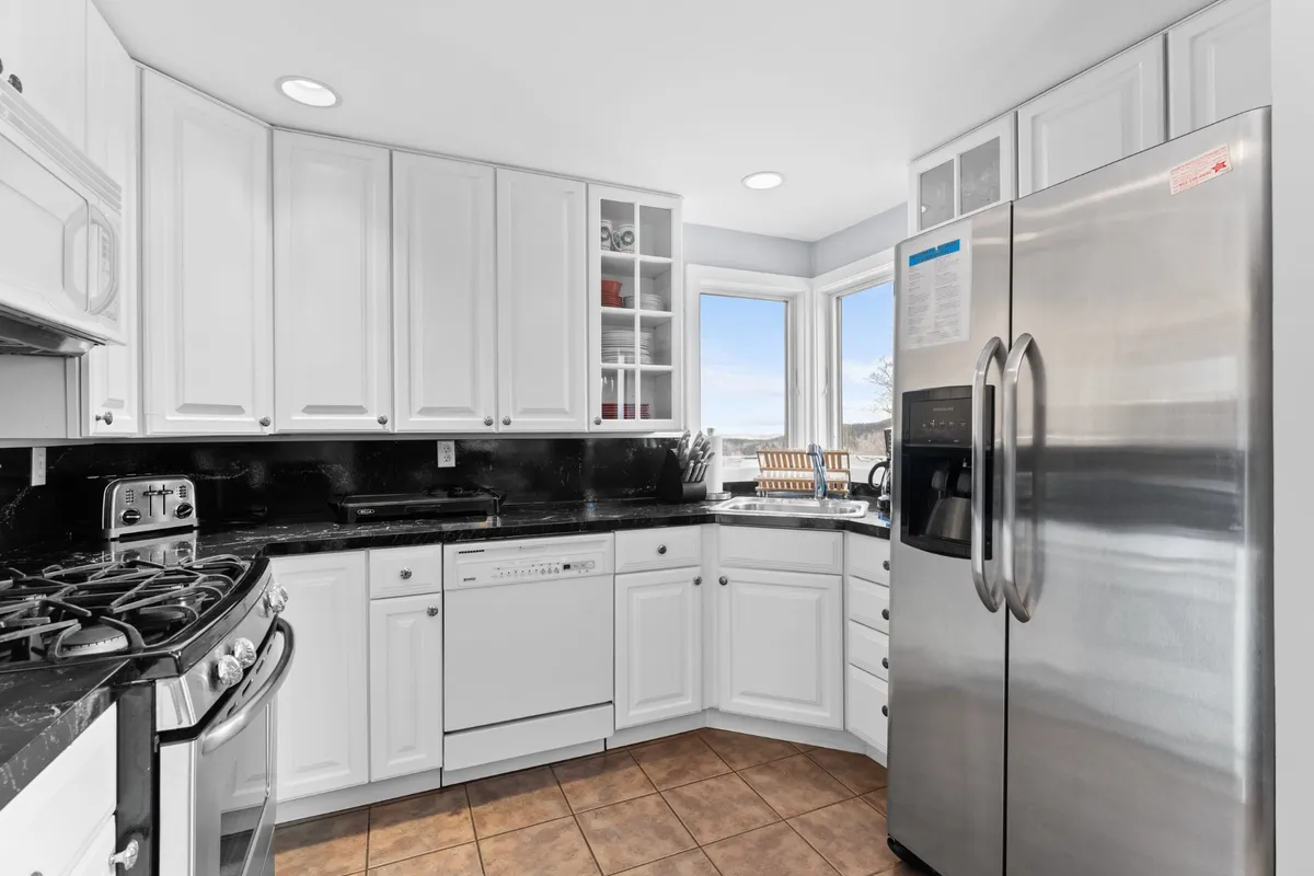 A bright, well-appointed kitchen with stainless steel appliances, black granite countertops, white cabinetry, and a window offering a scenic view. The space exudes warmth and is perfect for home-cooked meals, small dinner parties, or gathering with friends before heading out.