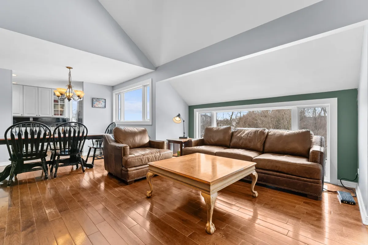 A cozy living room with leather sofas, a wooden coffee table, and large windows letting in abundant natural light. The space is ideal for relaxing, reading, or enjoying conversation against the backdrop of scenic views.